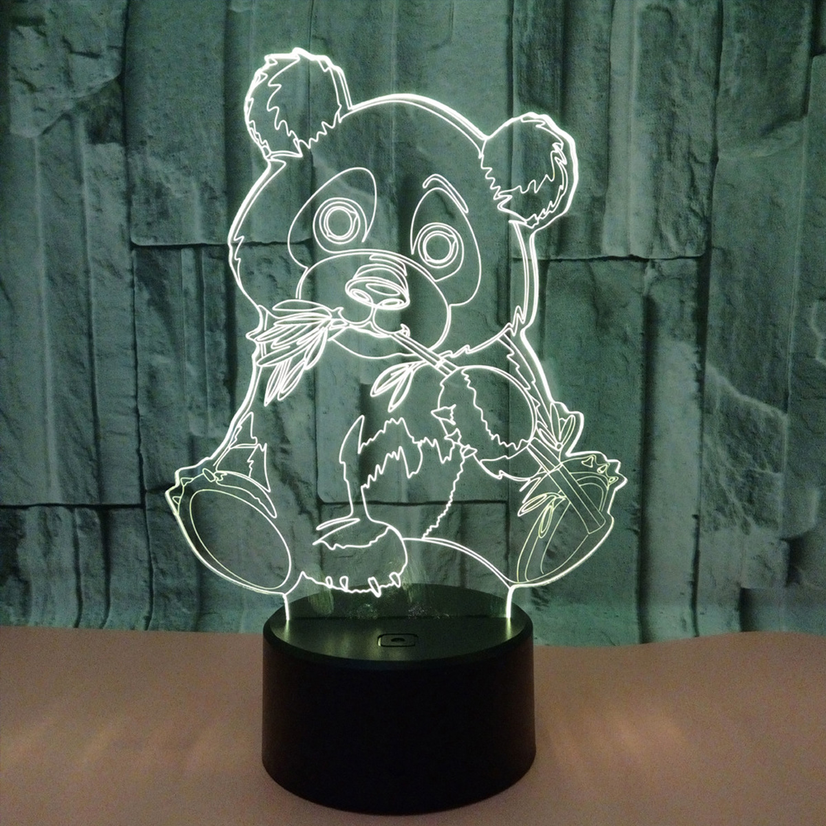 Eine pandaförmige Lampe leuchtet, die Bambus hält. Sie steht auf einem schwarzen Sockel vor einer strukturierten, graugrünen Wand.