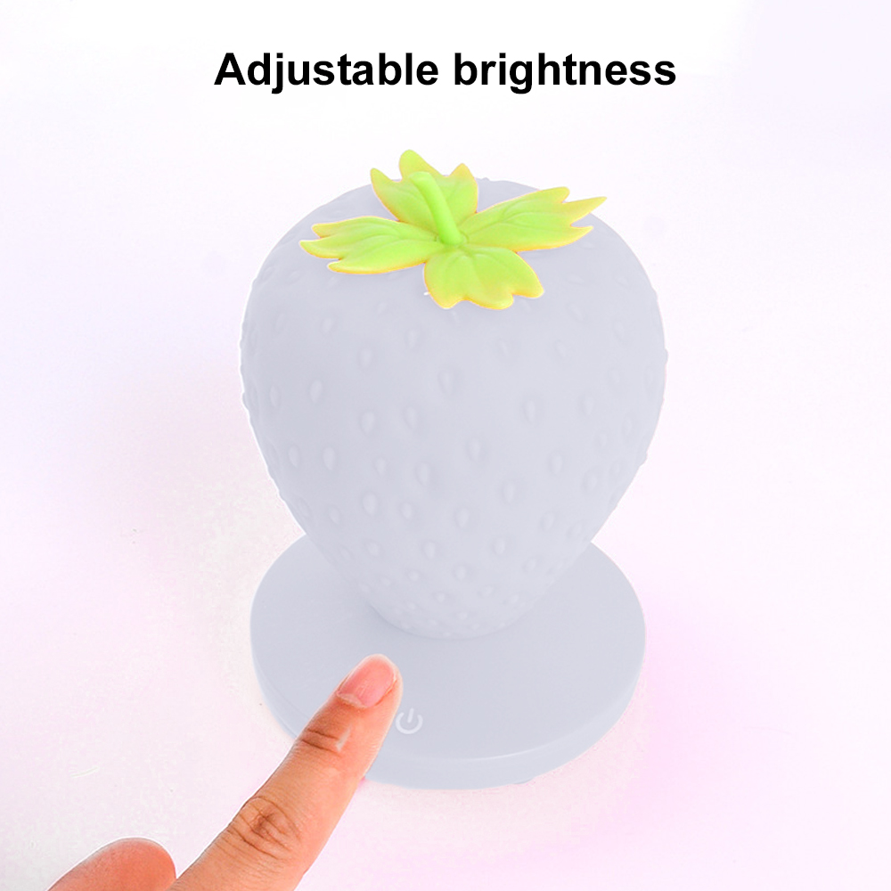 Eine weiße erdbeerförmige Lampe mit grünen Blättern. Ein Finger berührt die Basis. Text darüber lautet 'Einstellbare Helligkeit'.