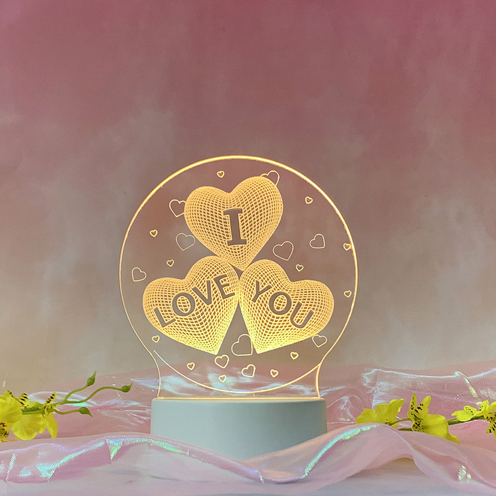Eine leuchtende herzförmige Lampe mit der Aufschrift „I LOVE YOU“. Rosa und weißer Hintergrund mit Blumen und reflektierendem Stoff.