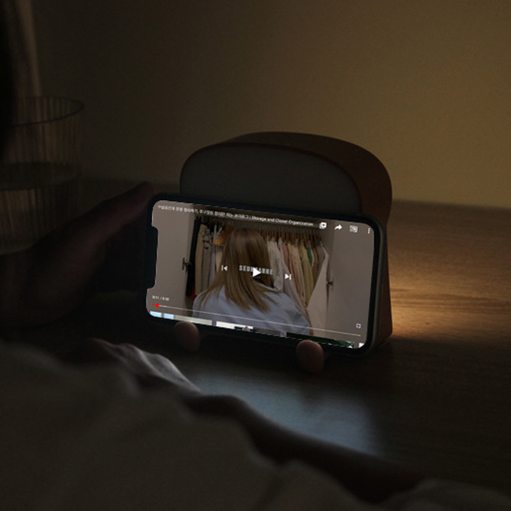 Eine Person hält ein Telefon in einem Ständer. Das Telefon zeigt ein Video einer Person vor einem Schrank mit Kleidung.