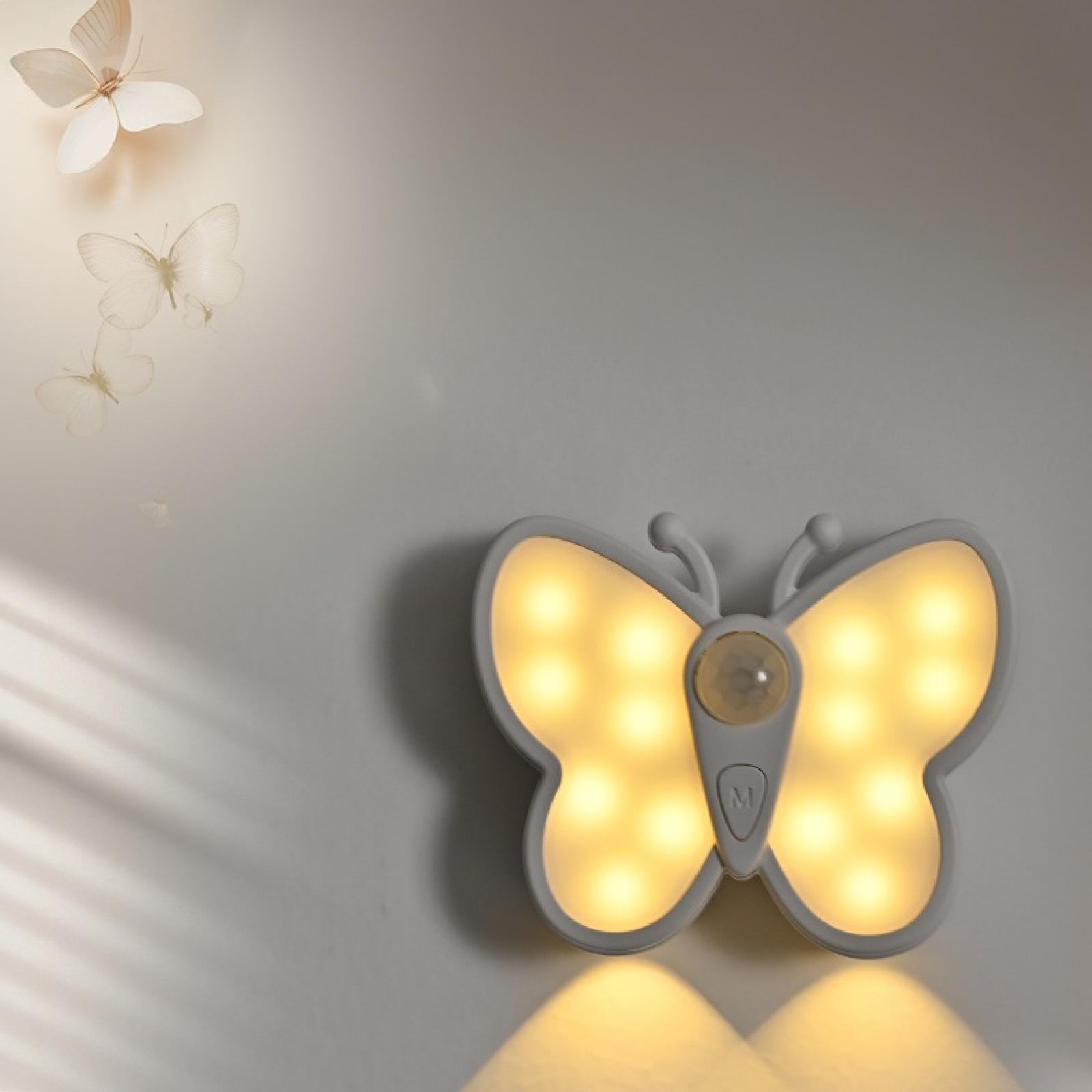 Ein schmetterlingsförmiges Nachtlicht an einer Wand, leuchtend. Schmetterlinge sind schwach darüber sichtbar. Licht scheint nach unten.