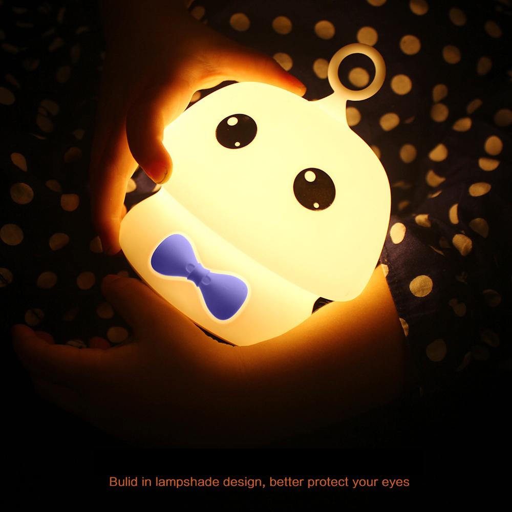 Eine leuchtende Cartoon-Käferlampe wird in Händen gehalten. Es hat schwarze Augen und eine blaue Fliege. Der Hintergrund ist ein gepunkteter Stoff.