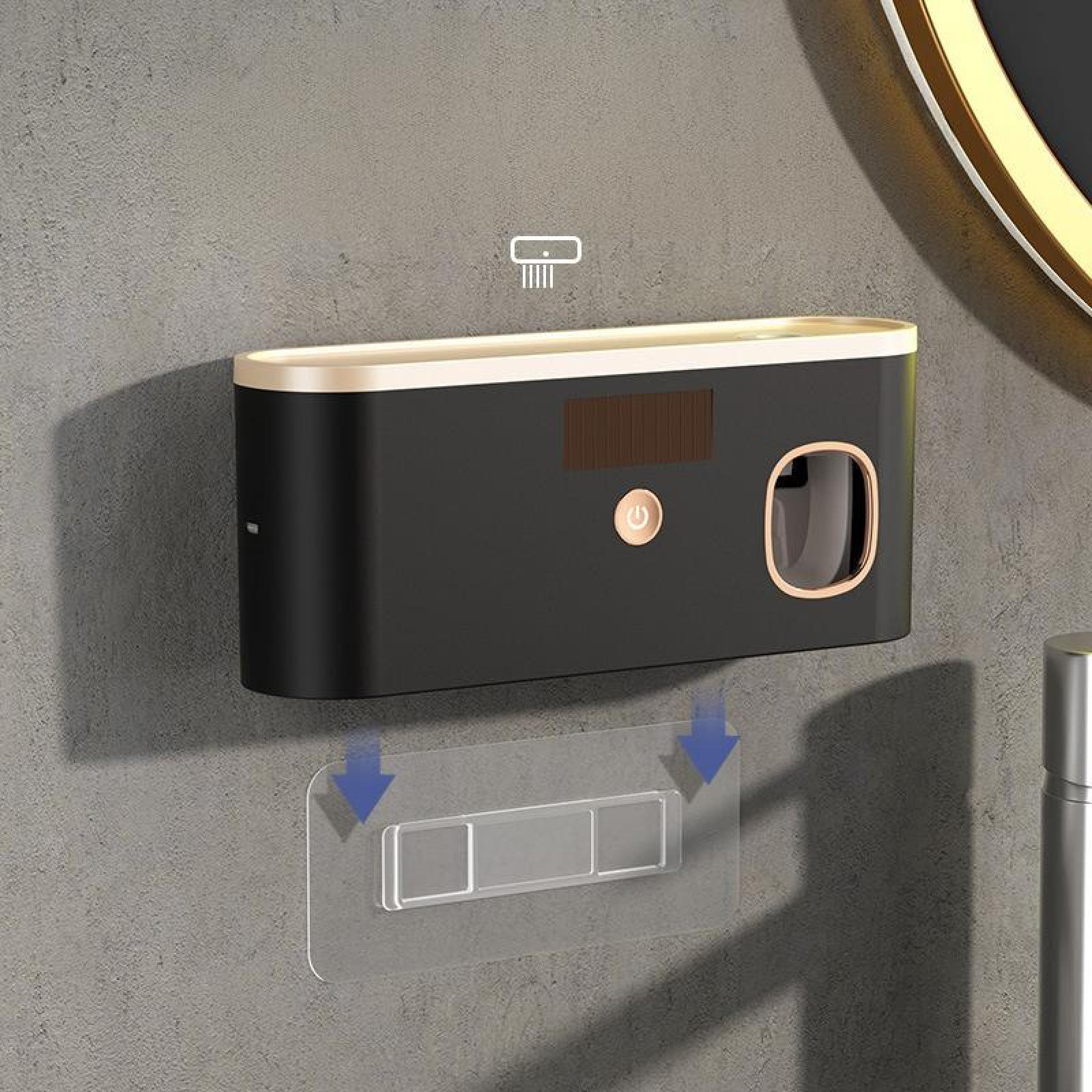 Ein schwarzer und goldener Zahnbürstenspender ist an einer grauen Wand montiert. Darunter befindet sich ein klarer Klebepads.