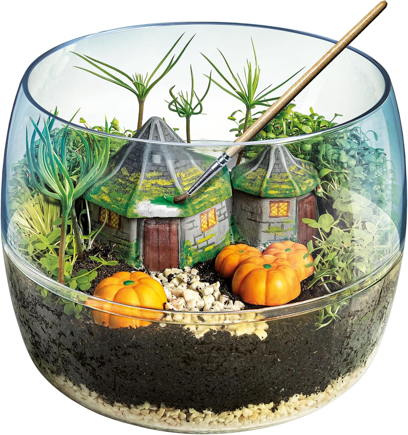 Un terrario con case in miniatura, zucche, piante e un pennello. Le case hanno tetti verdi, le zucche sono arancioni e le piante sono verdi.
