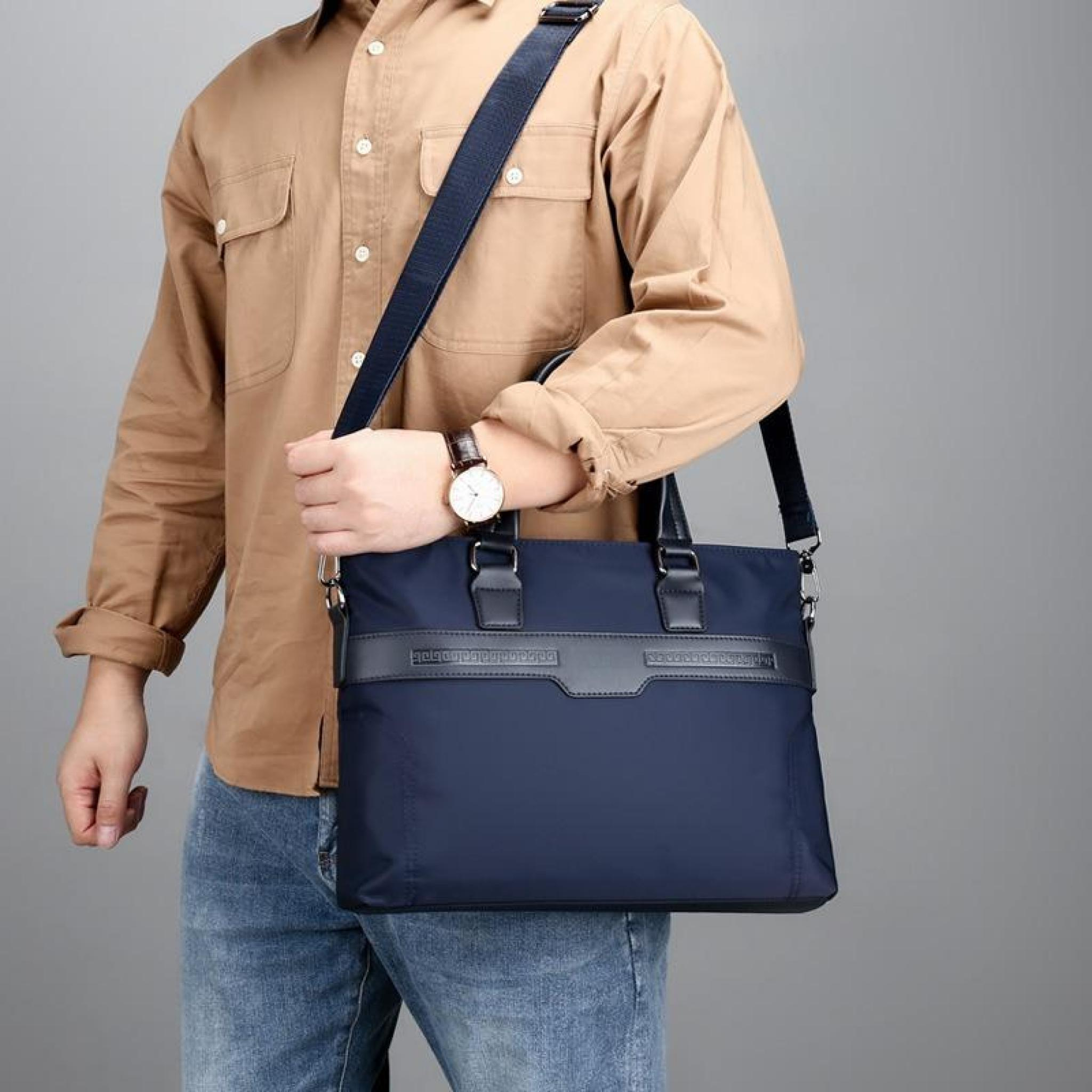 Mann in beigem Hemd und Jeans hält eine marineblaue Tasche. Eine Uhr ist an seinem Handgelenk. Grauer Hintergrund.