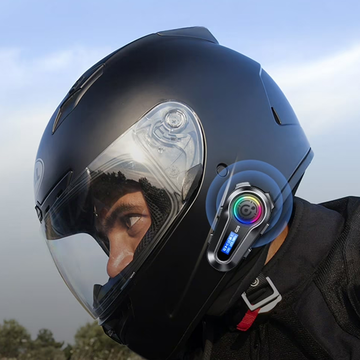 Eine Person trägt einen schwarzen Motorradhelm mit einem Kommunikationsgerät. Im Hintergrund ist ein klarer Himmel zu sehen.