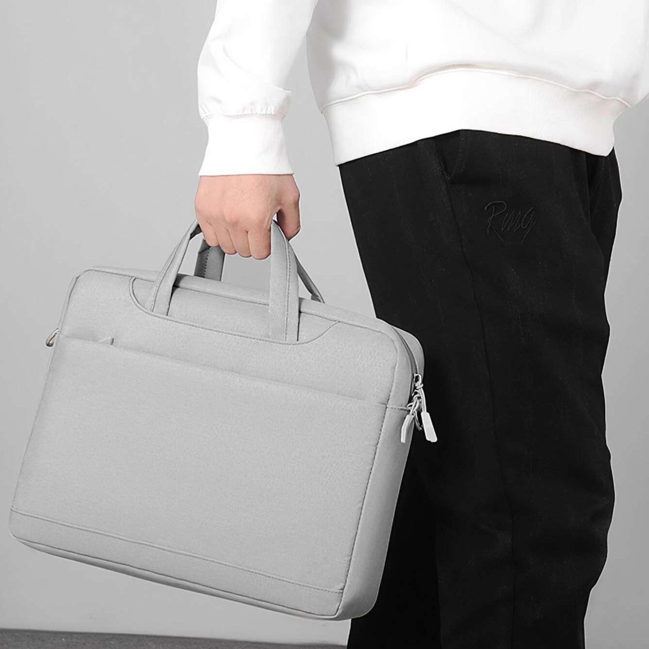 Person hält eine hellgraue Aktentasche. Sie tragen einen weißen Pullover und eine schwarze Hose. Der Hintergrund ist ein schlichtes Hellgrau.