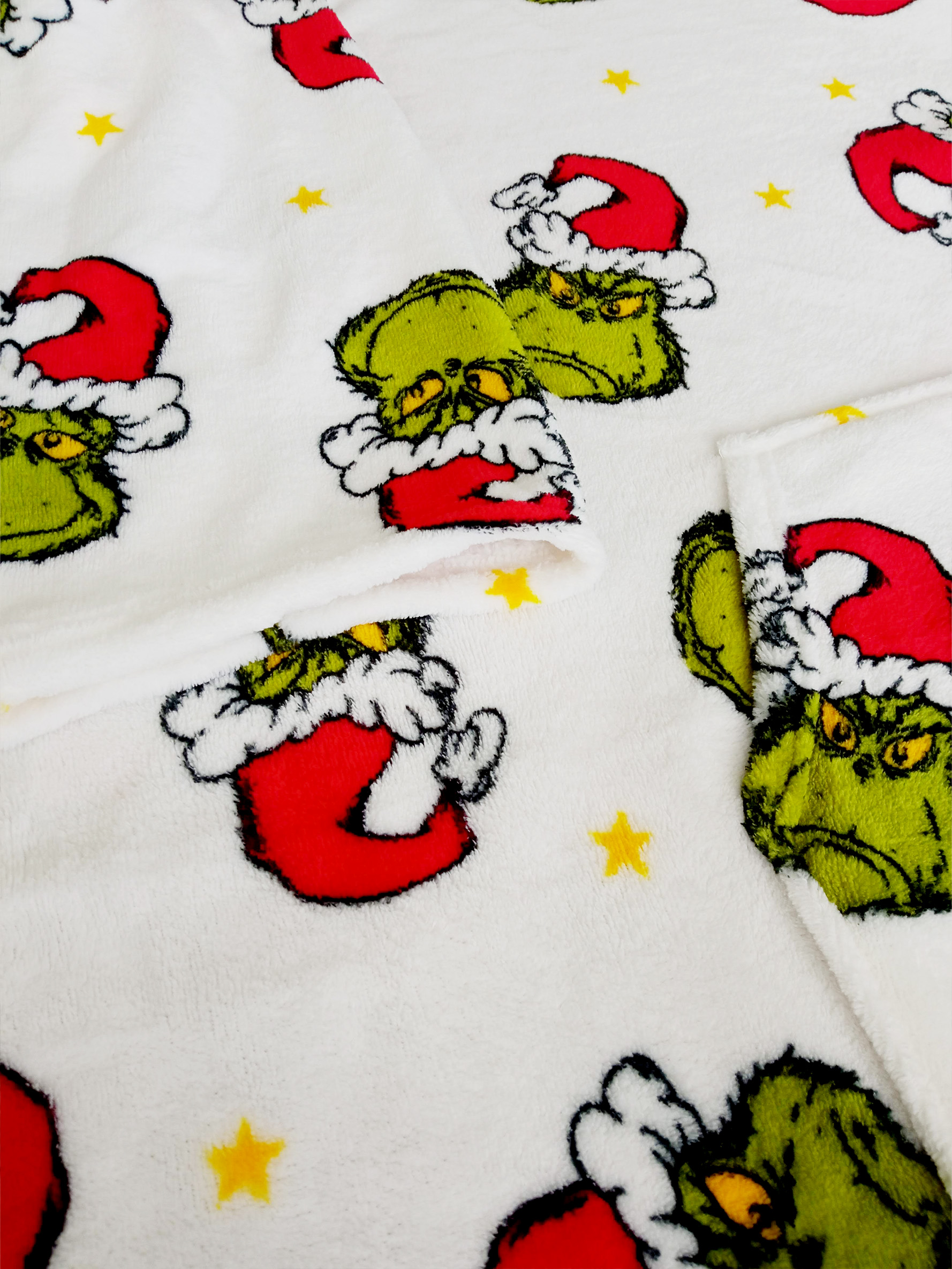 Weißer Stoff mit Grinch-Gesichtern, die Weihnachtsmützen und gelbe Sterne tragen.