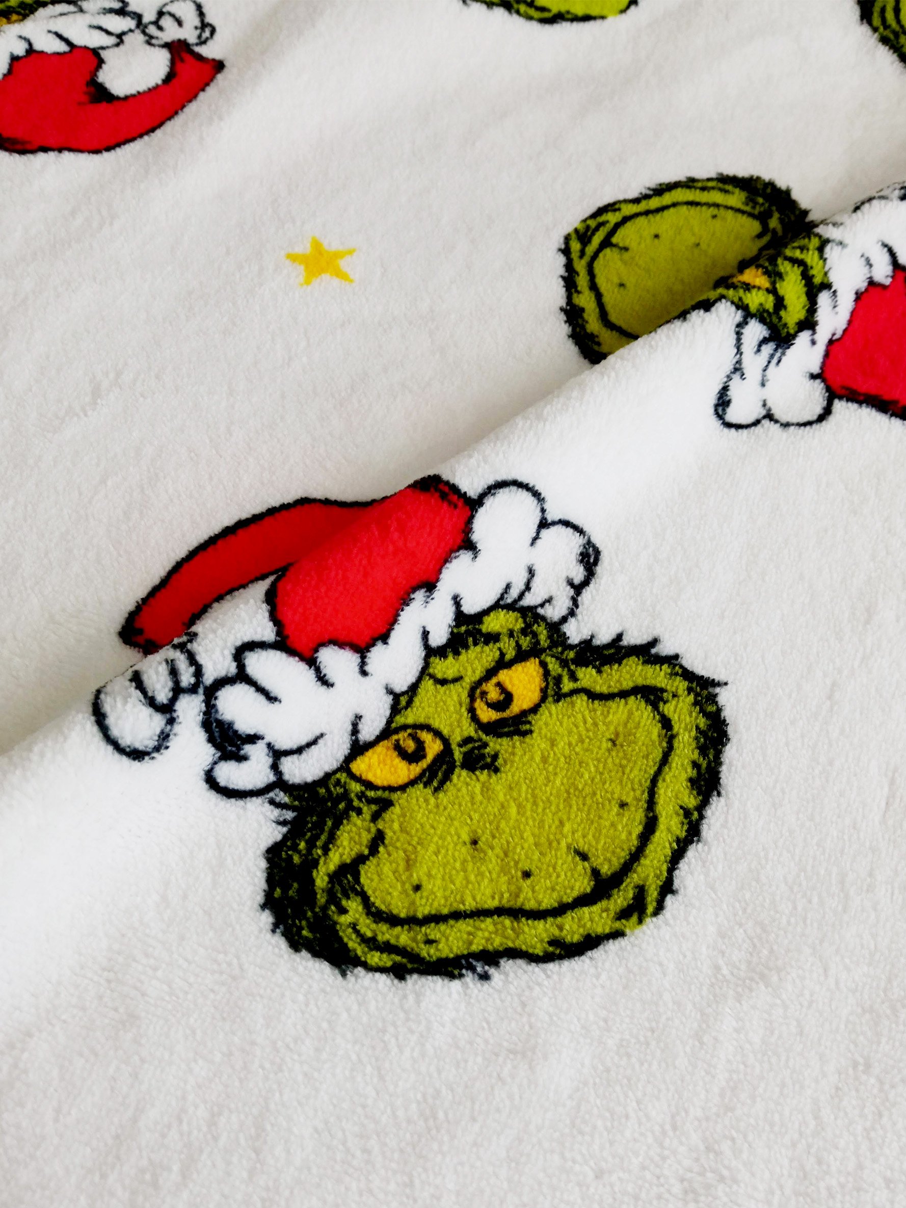 Weißer Stoff mit Grinch-Gesichtern, die Weihnachtsmützen tragen, und einem gelben Stern.