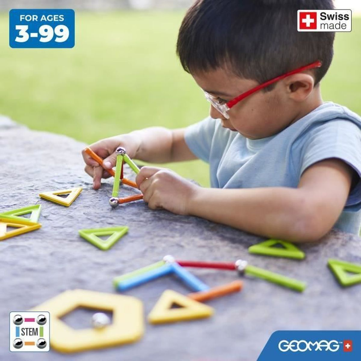 Un bambino con gli occhiali costruisce con giocattoli magnetici colorati su una superficie di pietra all'aperto.