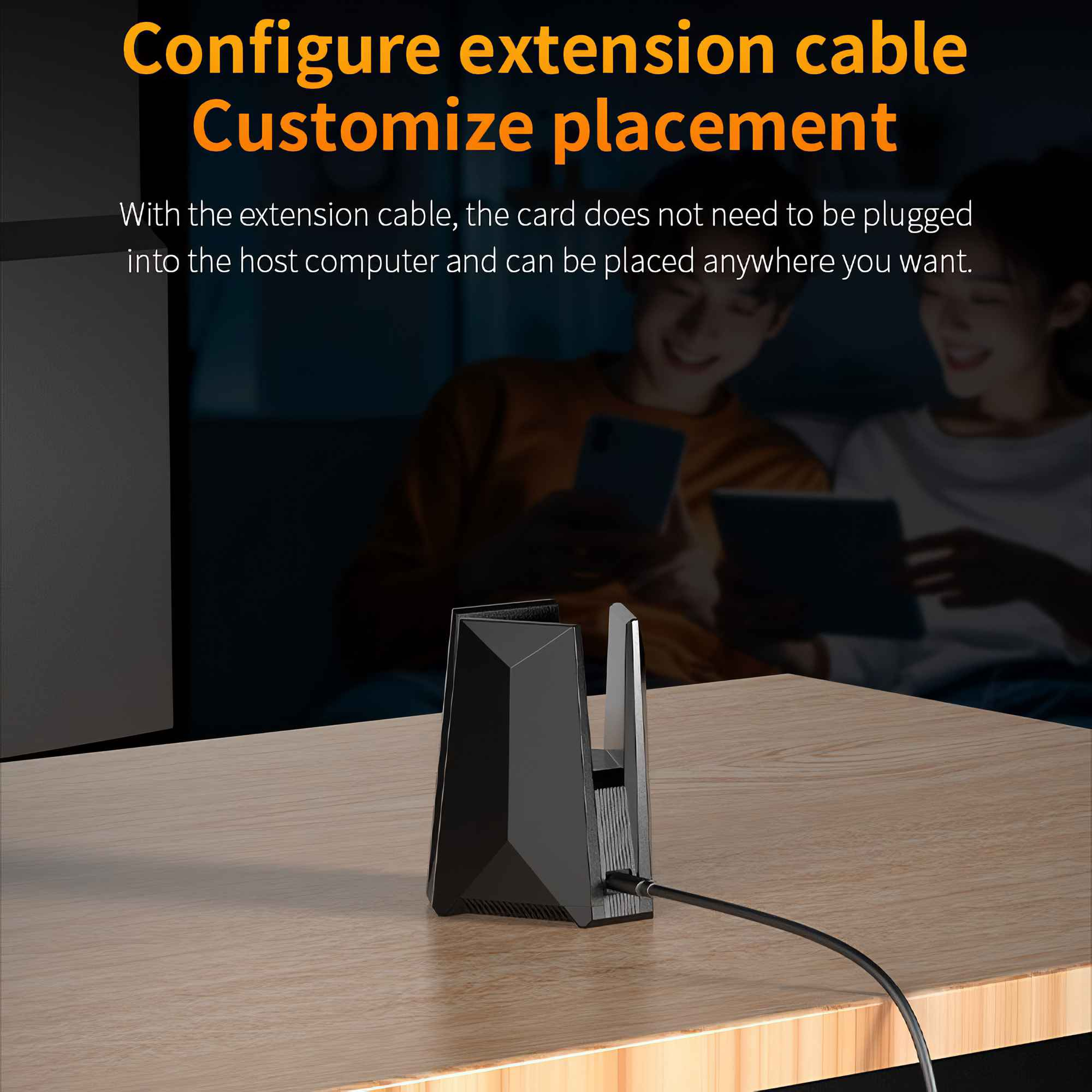 Ein schwarzes Gerät mit Kabel auf einem Holztisch. Im Hintergrund halten zwei Personen Tablets und lächeln.