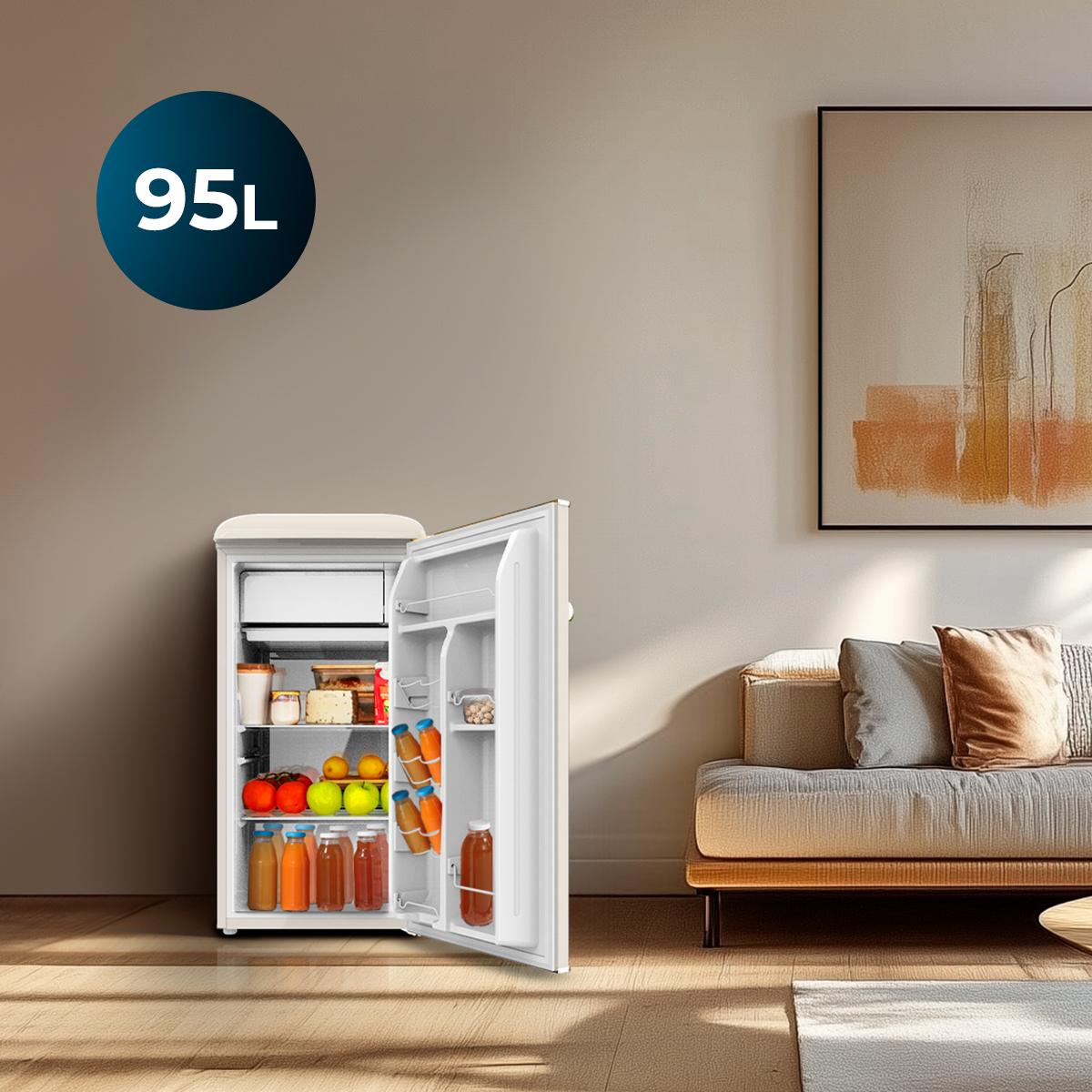 Mała lodówka jest otwarta, wypełniona owocami i napojami. W tle sofa i sztuka abstrakcyjna.