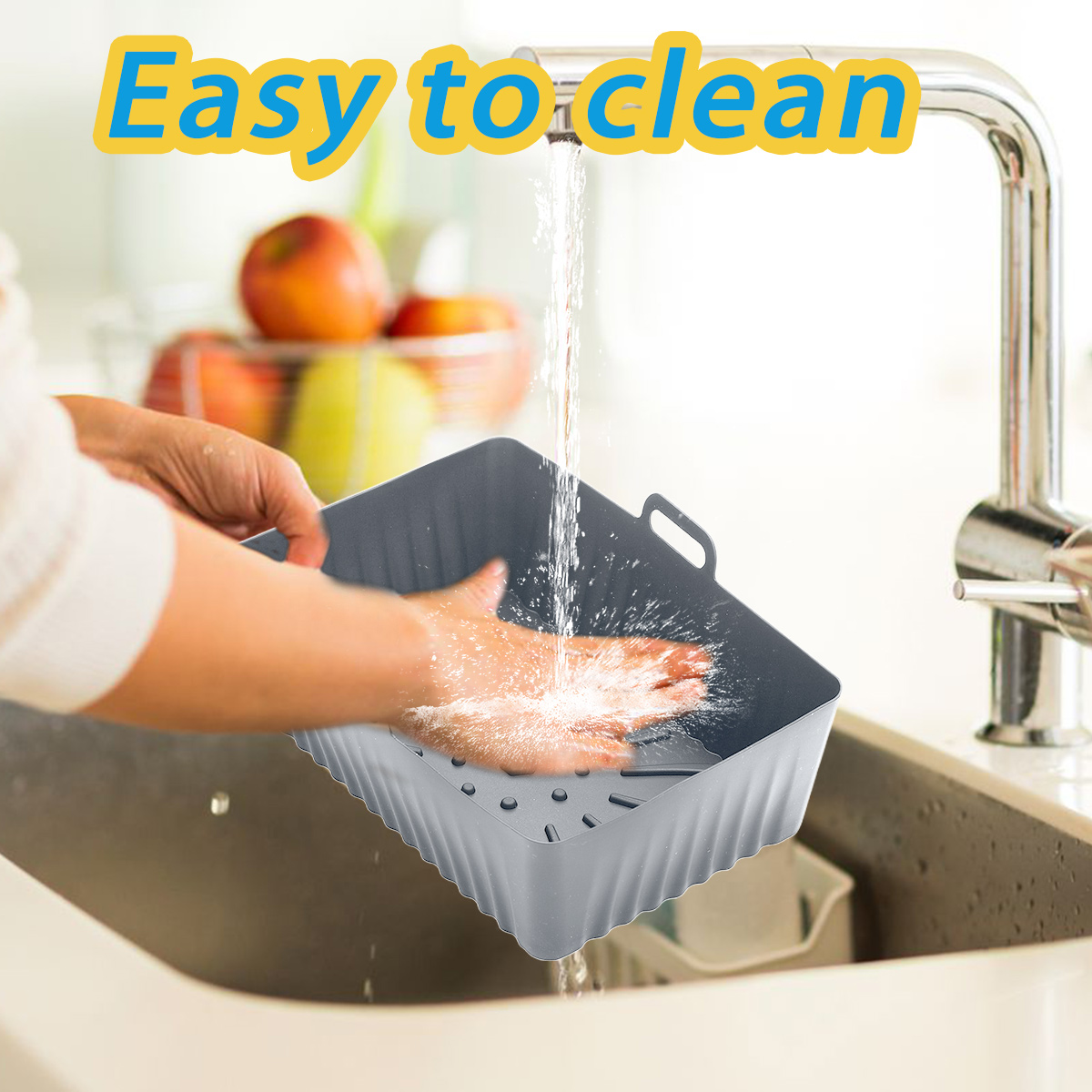 Eine Person wäscht einen grauen quadratischen Korb unter einem laufenden Wasserhahn. Wasser spritzt auf die Hand und den Korb. Früchte sind im Hintergrund.