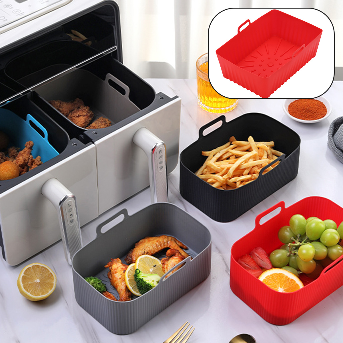 Ein Luftfritteuse mit Essen, umgeben von Tabletts mit frittiertem Essen, Früchten und einem roten Tablett. Eine Zitrone liegt auf dem Tisch.