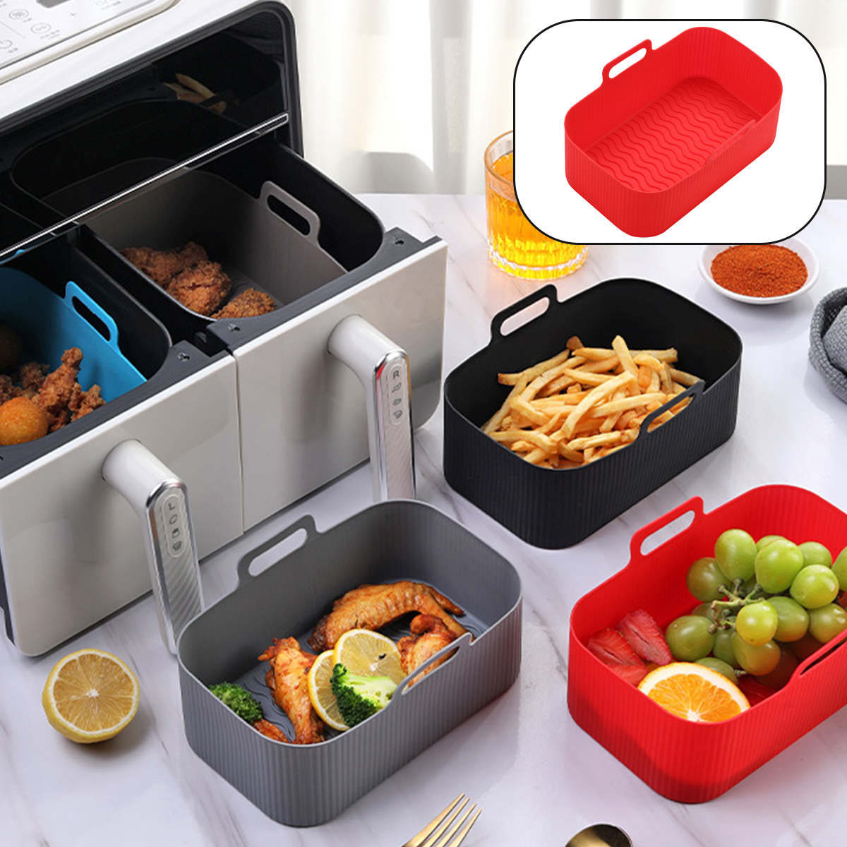 Ein Airfryer mit Tabletts mit Essen, Pommes, Hühnchen, Obst und einem roten Tablett. Auch ein Glas Saft, eine Schüssel mit Gewürzen und eine Zitrone.