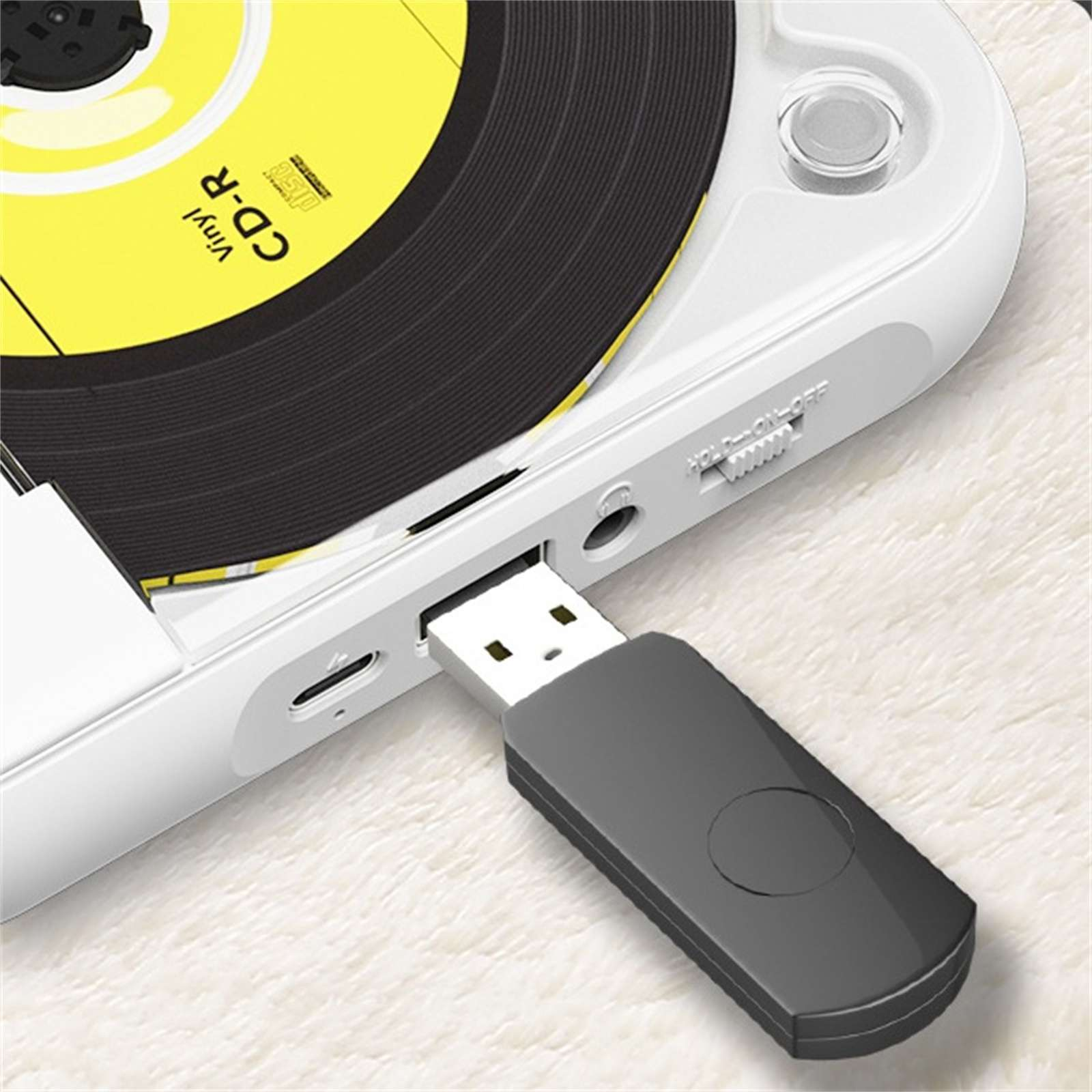 Ein weißer CD-Player mit einem eingesteckten USB-Gerät. Es befindet sich auf einer weißen, flauschigen Oberfläche. Der CD-Player hat ein Vinyl-ähnliches Design.