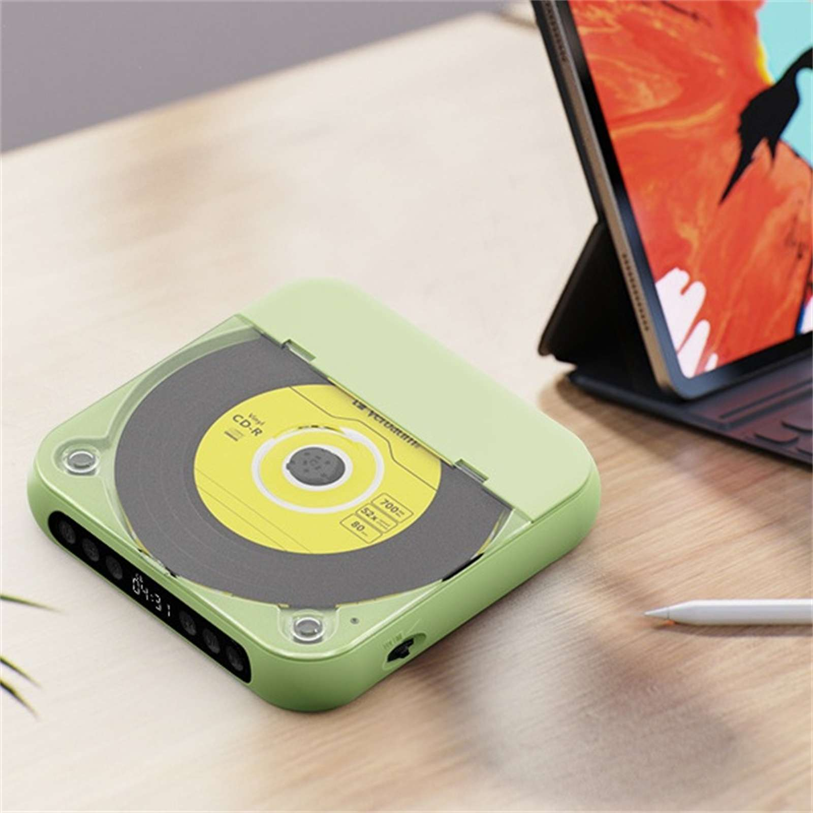 Ein grüner CD-Player mit einer CD, ein Tablet auf einem Ständer und ein Stift auf einer Holzoberfläche.