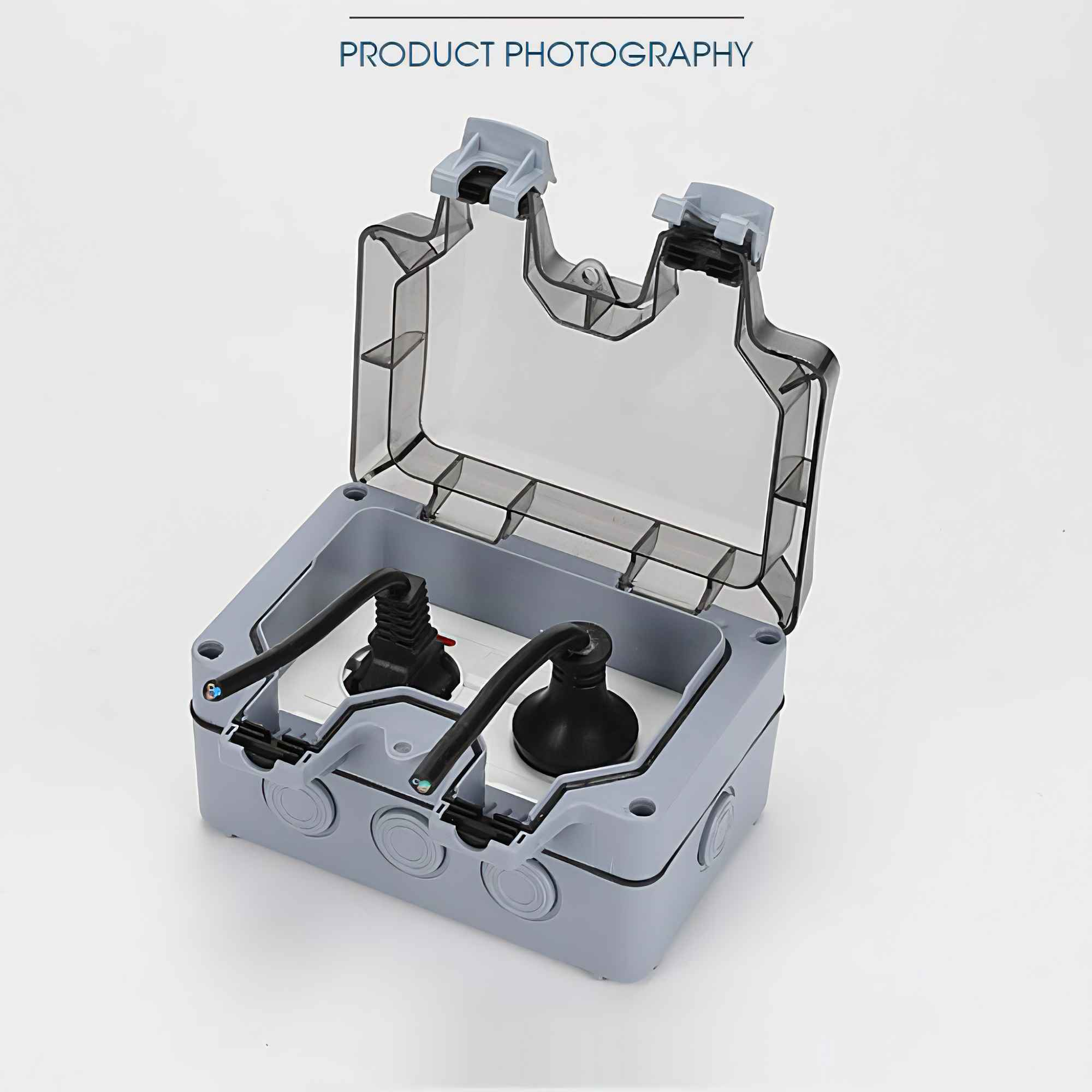 Graue elektrische Anschlussdose mit transparentem Deckel, enthält zwei schwarze Stecker. Produktfotografie auf weißem Hintergrund.