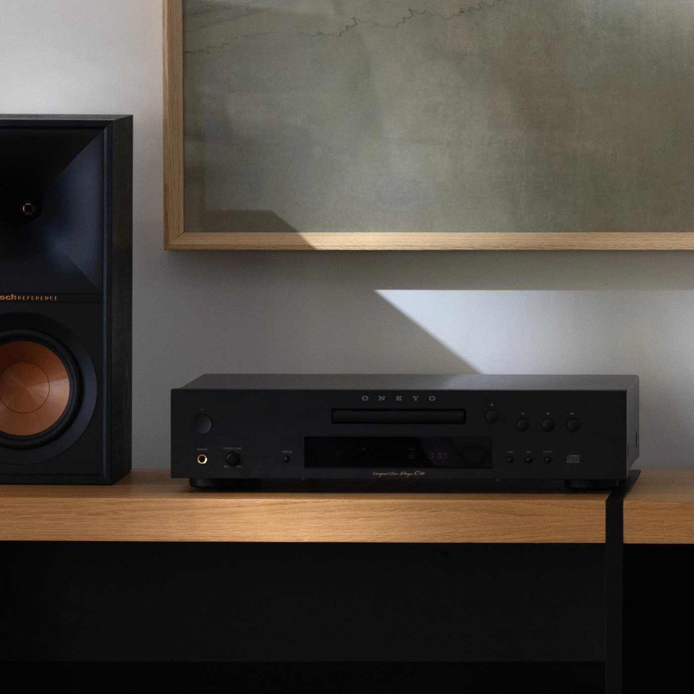 Ein schwarzes Stereoanlage steht auf einem Holzregal. Ein Lautsprecher und ein CD-Player sind sichtbar. Ein gerahmtes Bild hängt oben.