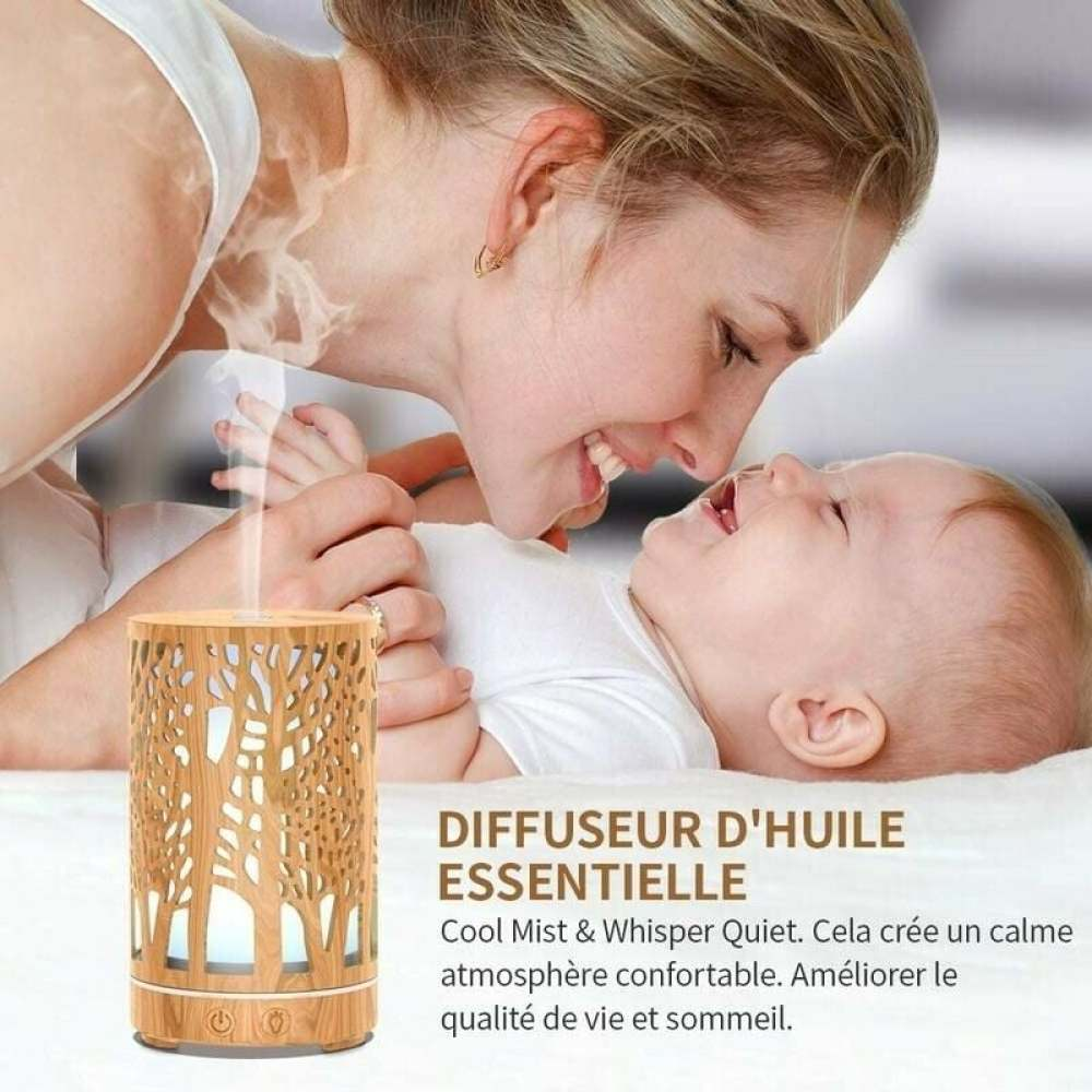 Eine Mutter lächelt ein Baby an. Ein ätherischer Holzöldiffusor befindet sich im Vordergrund. Text: DIFFUSEUR D'HUILE ESSENTIELLE.