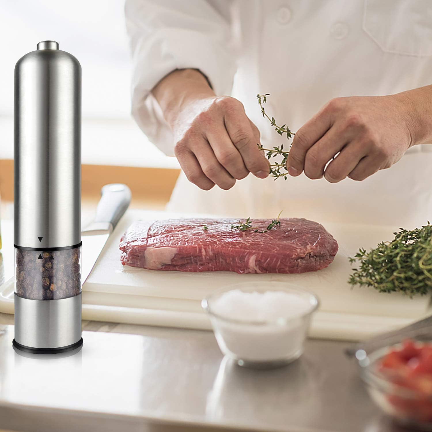 Ein Koch bereitet ein Steak zu. Links ist eine Pfeffermühle aus Edelstahl. Thymian und Salz sind im Vordergrund, mit einem rohen Steak.