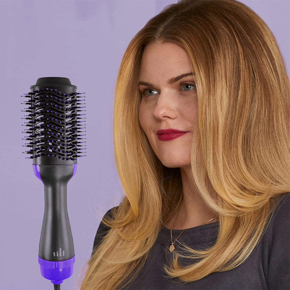 Eine Frau mit blondem Haar hält einen Haarstyler. Der Styler ist schwarz und lila. Sie trägt ein graues Hemd und eine goldene Halskette.
