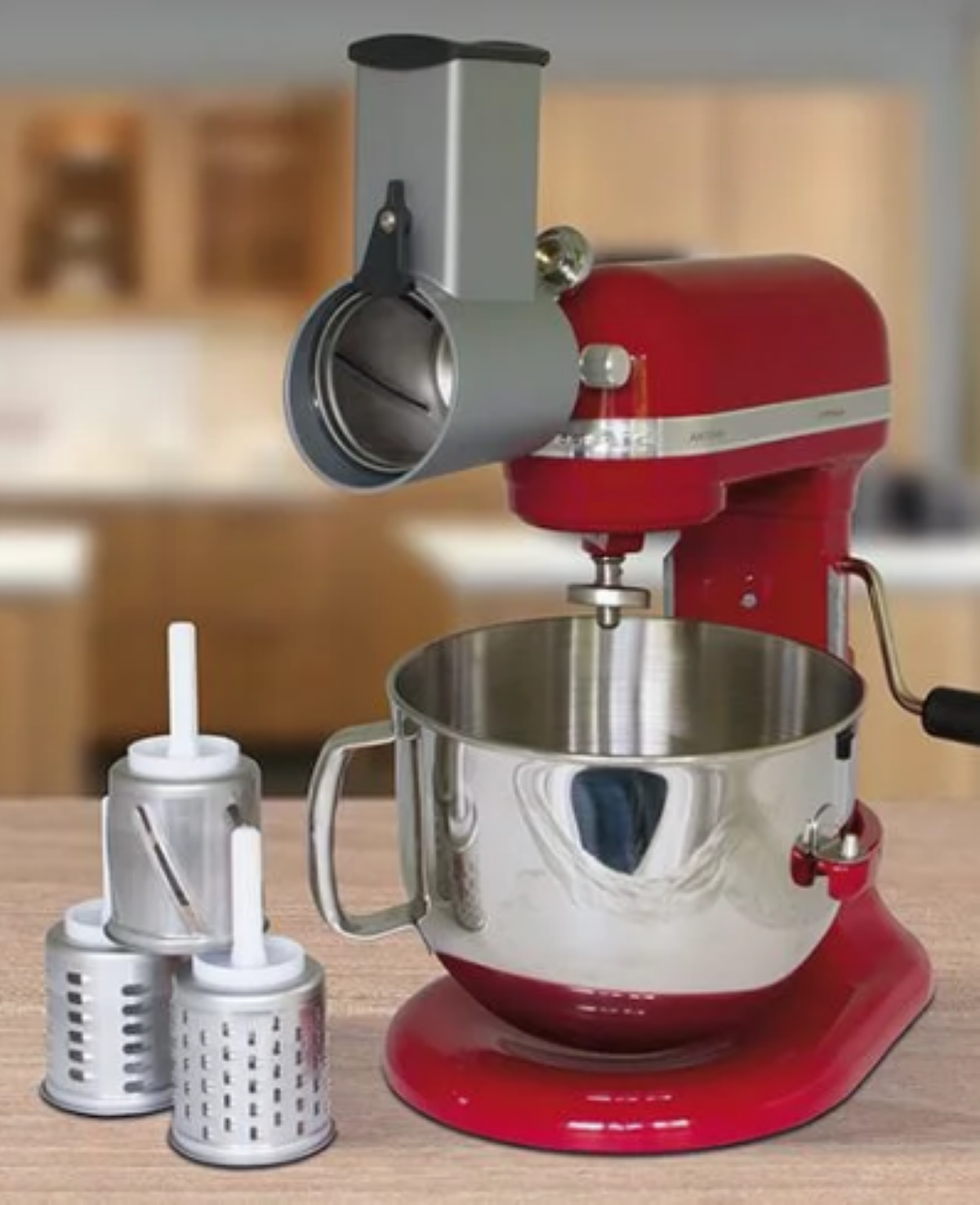 Ein roter Küchenmixer mit einem Reibeaufsatz und mehreren Reiben. Eine Edelstahlschüssel ist befestigt. Der Hintergrund ist eine Küche.