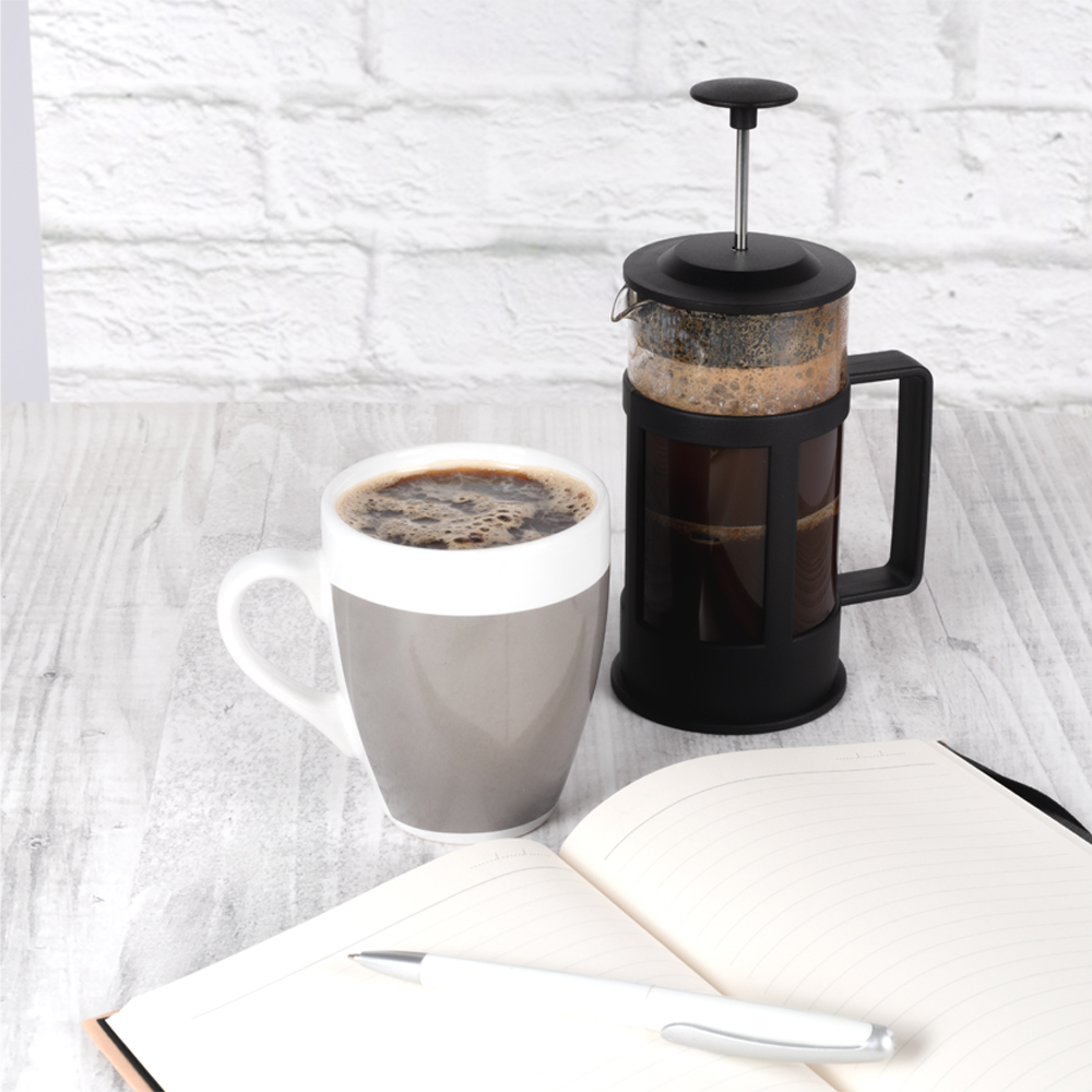 Ahşap bir masada kahve fincanı ve French press, açık bir defter ve kalem.