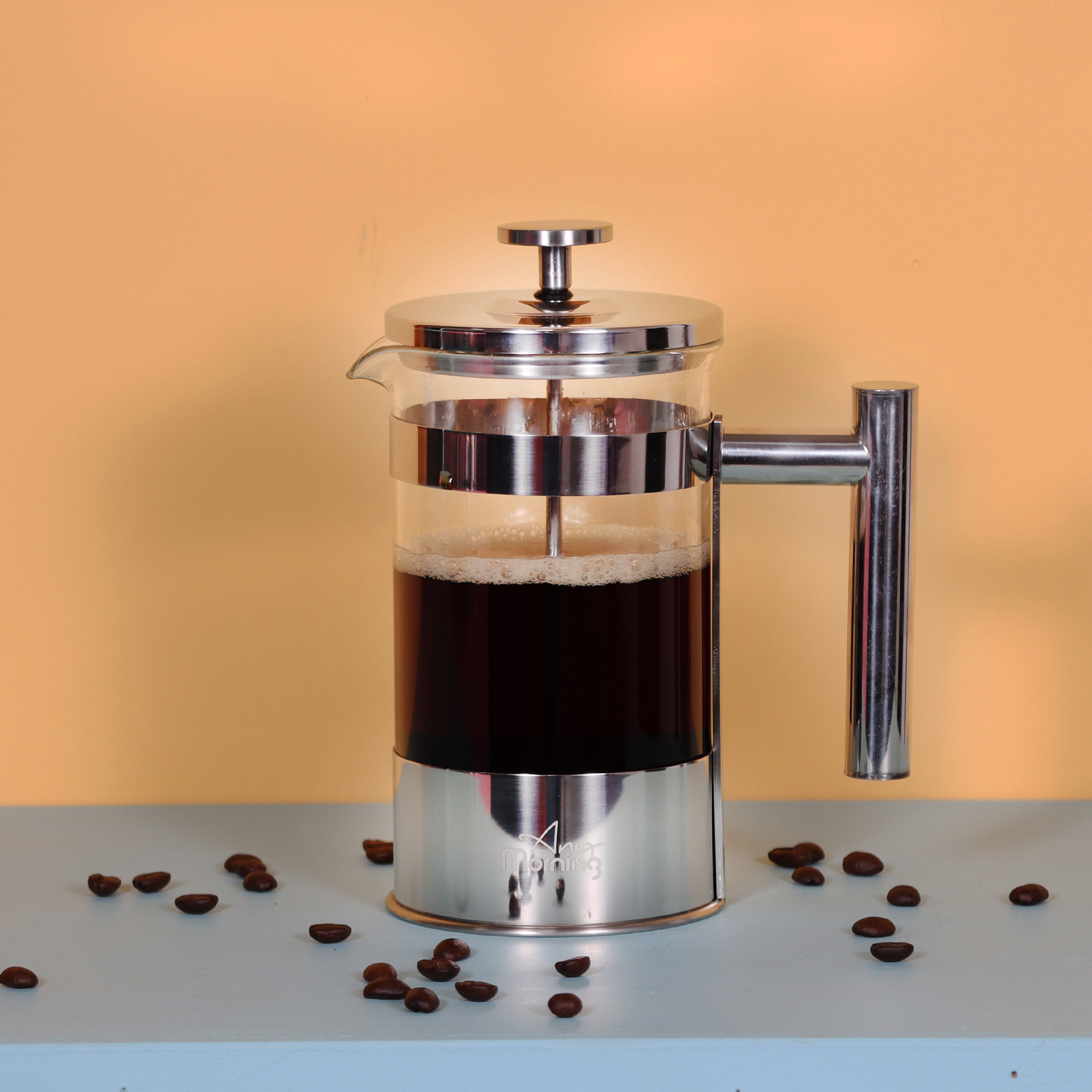 Una prensa francesa con café está sobre una superficie azul claro con granos de café esparcidos. El fondo es amarillo.