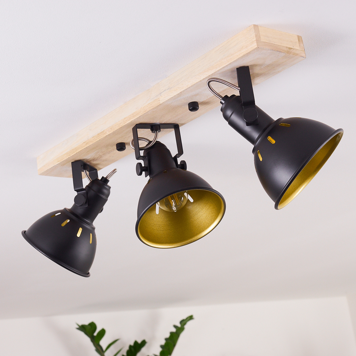 Eine Deckenleuchte mit drei schwarzen Strahlern mit goldenen Innenräumen, die an einem Holzbalken befestigt sind.