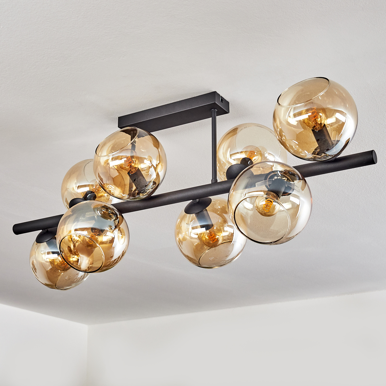 Eine moderne Deckenleuchte mit kugelförmigen, bernsteinfarbenen Glasschirmen. Sie hat einen schwarzen Metallrahmen und ist an einer weißen Decke montiert.