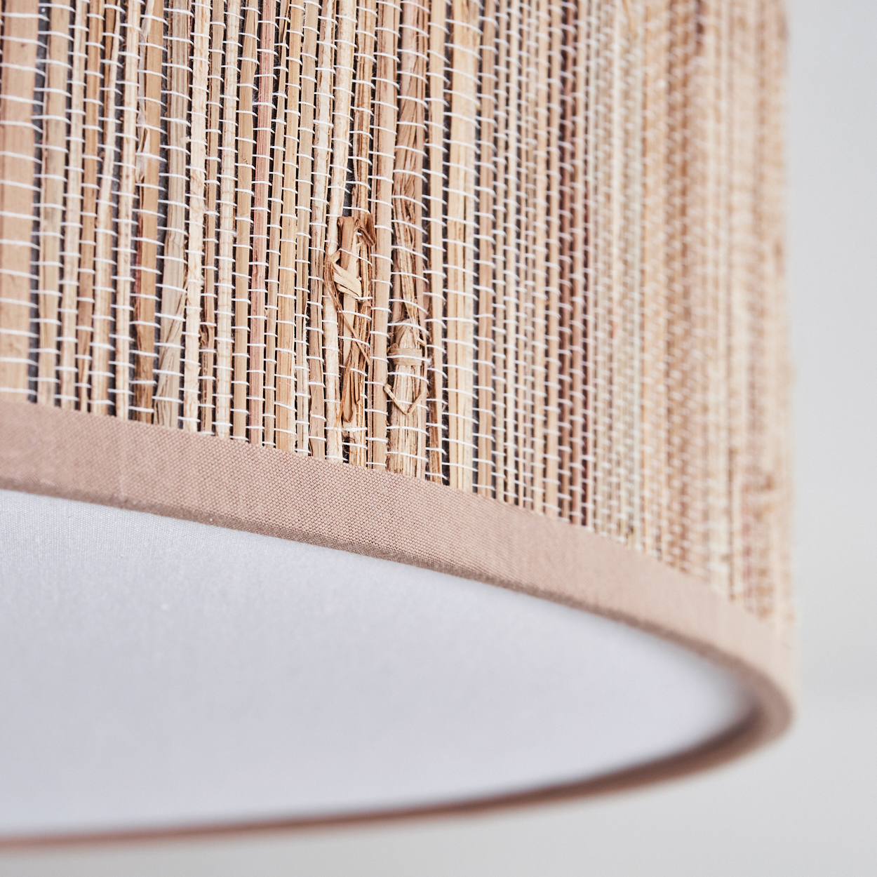 Nahaufnahme eines Lampenschirms. Er hat einen gewebten, beigefarbenen oberen Teil und einen weißen unteren Teil. Der beige Abschnitt hat einen braunen Stoffrand.