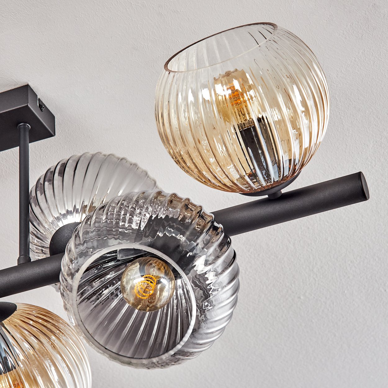 Moderne Deckenleuchte mit Glas-Globus in Bernstein und Klar. Die Leuchte hat einen schwarzen Metallrahmen und sichtbare Glühbirnen.