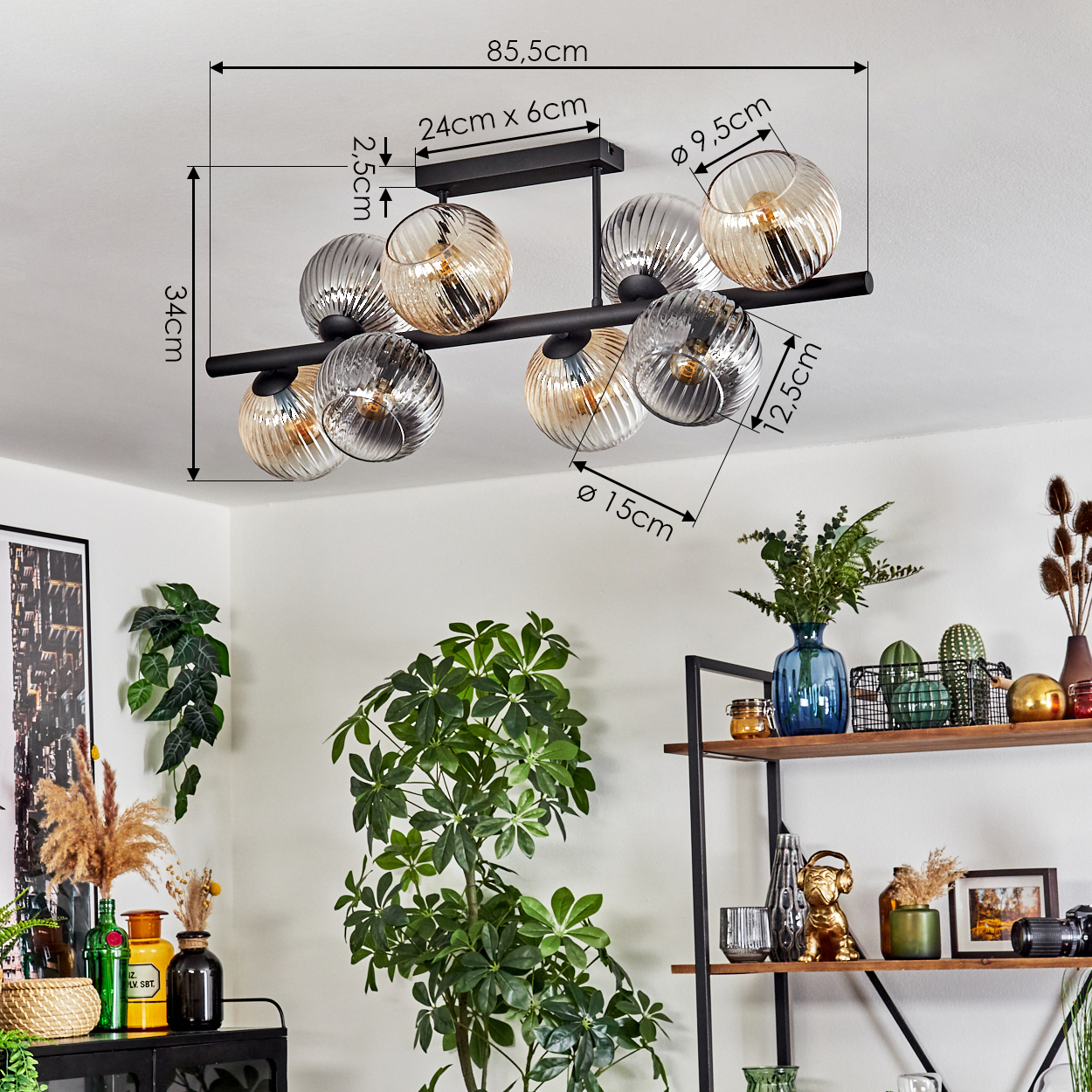 Eine moderne Deckenlampe mit Glaskugeln, Maße beschriftet. Der Raum hat Pflanzen und ein Regal mit Dekorationen.