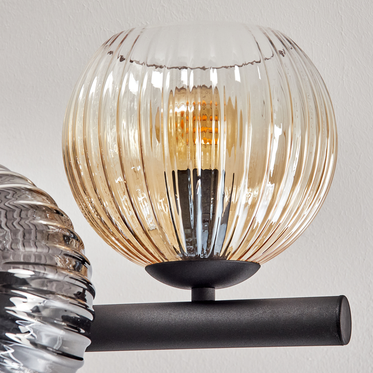 Nahaufnahme einer modernen Lampe. Sie hat einen runden, geriffelten Glasschirm mit einer warmen Glühbirne im Inneren, montiert auf einem schwarzen Metallarm.