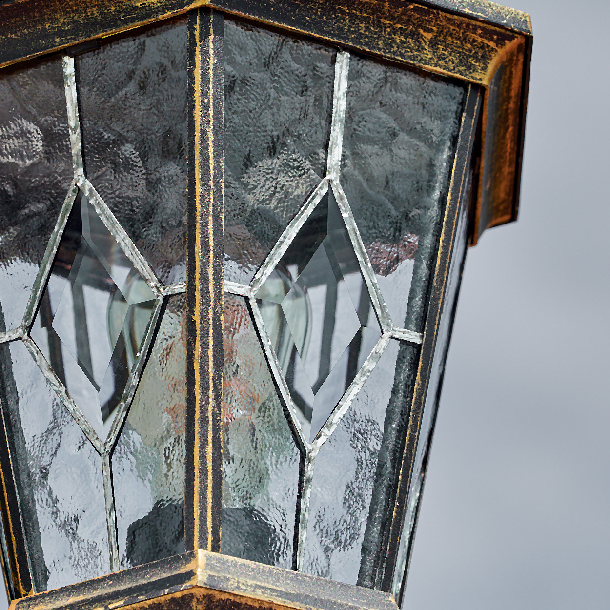 Nahaufnahme einer dekorativen Lampe. Sie hat rautenförmige Glasscheiben mit strukturierter Oberfläche. Der Rahmen ist schwarz und gold.