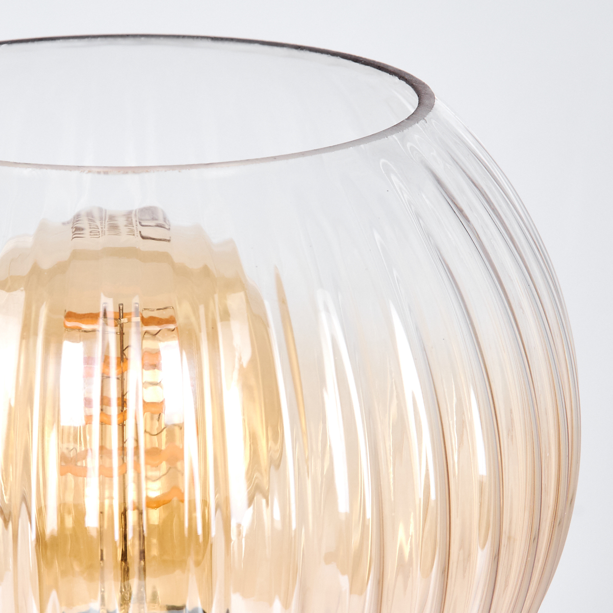 Nahaufnahme einer Glaslampe. Die Lampe ist rund mit vertikalen Rippen. Im Inneren befindet sich eine orangefarbene Glühbirne.