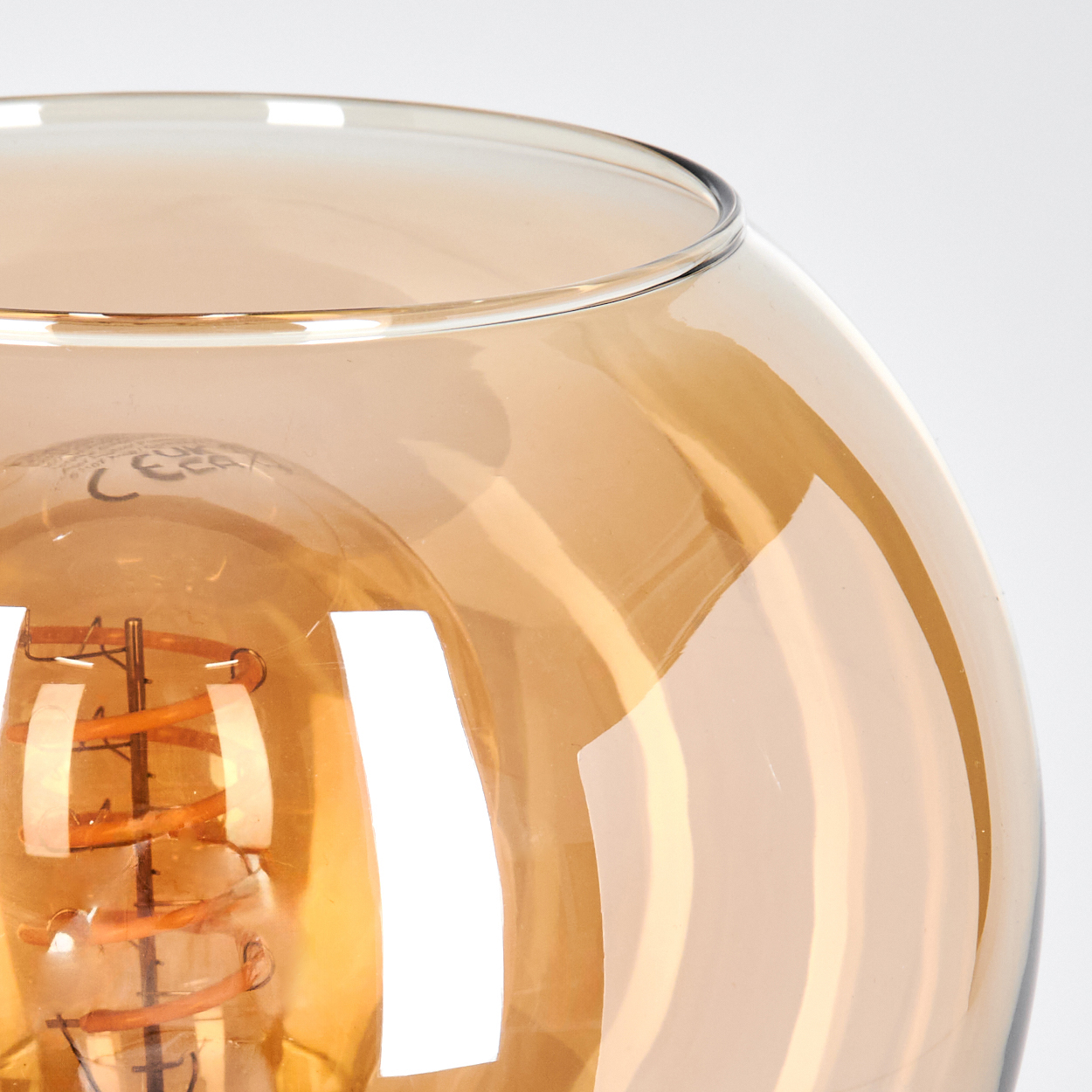Nahaufnahme einer Glasleuchte mit einer Glühbirne im Inneren. Das Glas ist bernsteinfarben und die Glühbirne leuchtet.