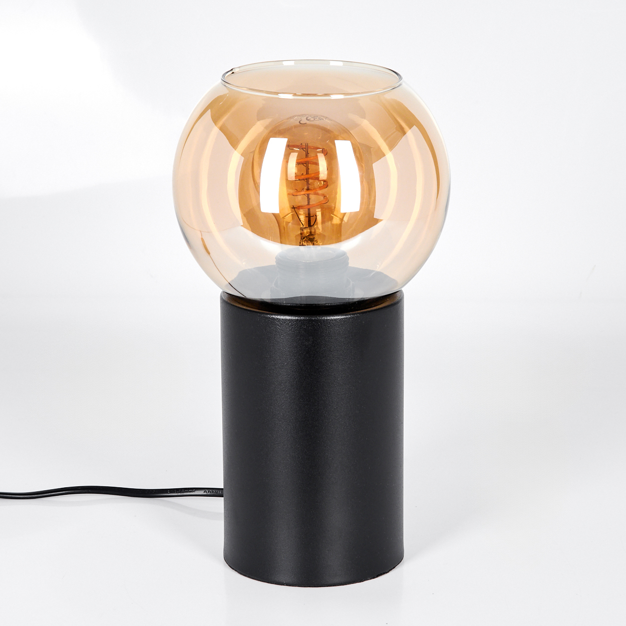 Eine moderne Lampe mit schwarzem zylindrischen Sockel und kugelförmigem bernsteinfarbenem Glasschirm. Die Glühbirne ist sichtbar.
