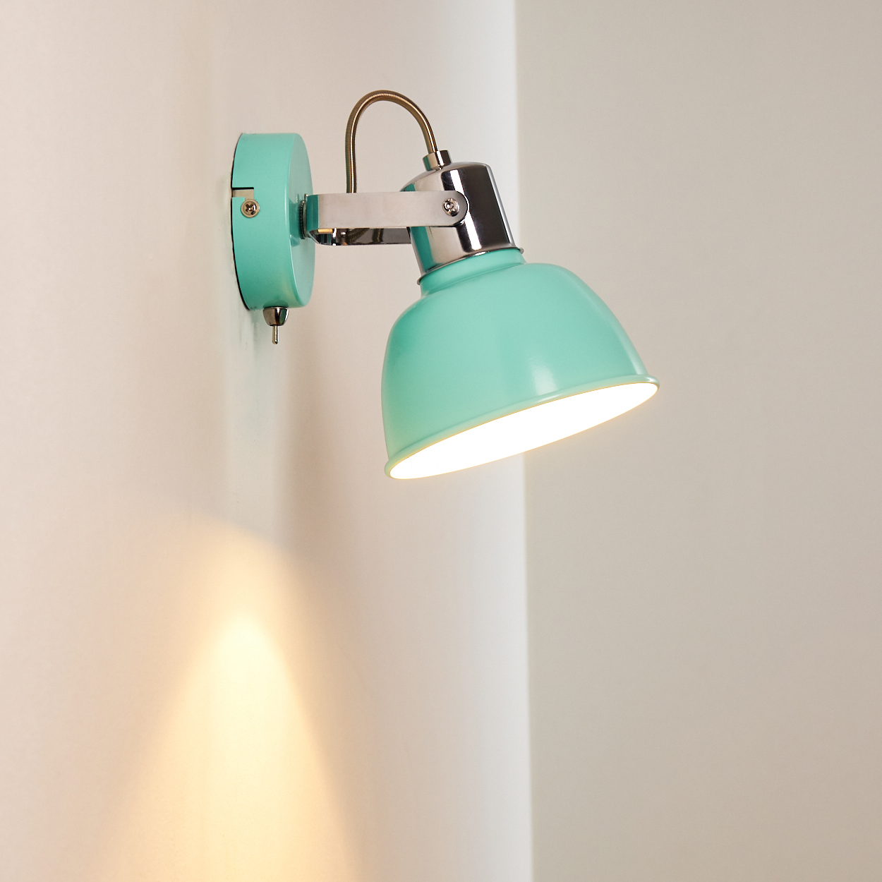 Eine mintgrüne Wandleuchte ist an einer weißen Wand befestigt. Die Lampe ist eingeschaltet und wirft ein warmes Licht nach unten.