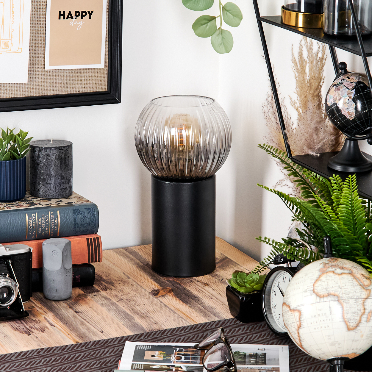 Ein Schreibtisch mit Lampe, Büchern, Kamera, Globus und Uhr. Der Hintergrund hat ein Regal mit Globus und Pflanzen.