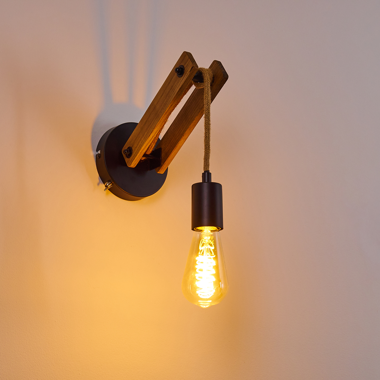 Eine Wandlampe aus Holz mit einer hängenden Glühbirne leuchtet vor einer hellen Wand. Die Lampe hat einen Metallsockel.