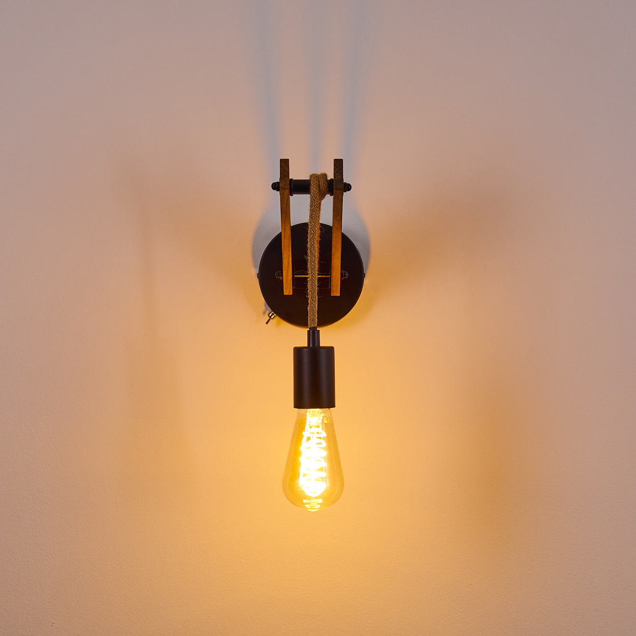 Eine Wandleuchte mit schwarzem Sockel, Holzakzenten und einer glühenden Edison-Glühbirne vor einer beigen Wand.