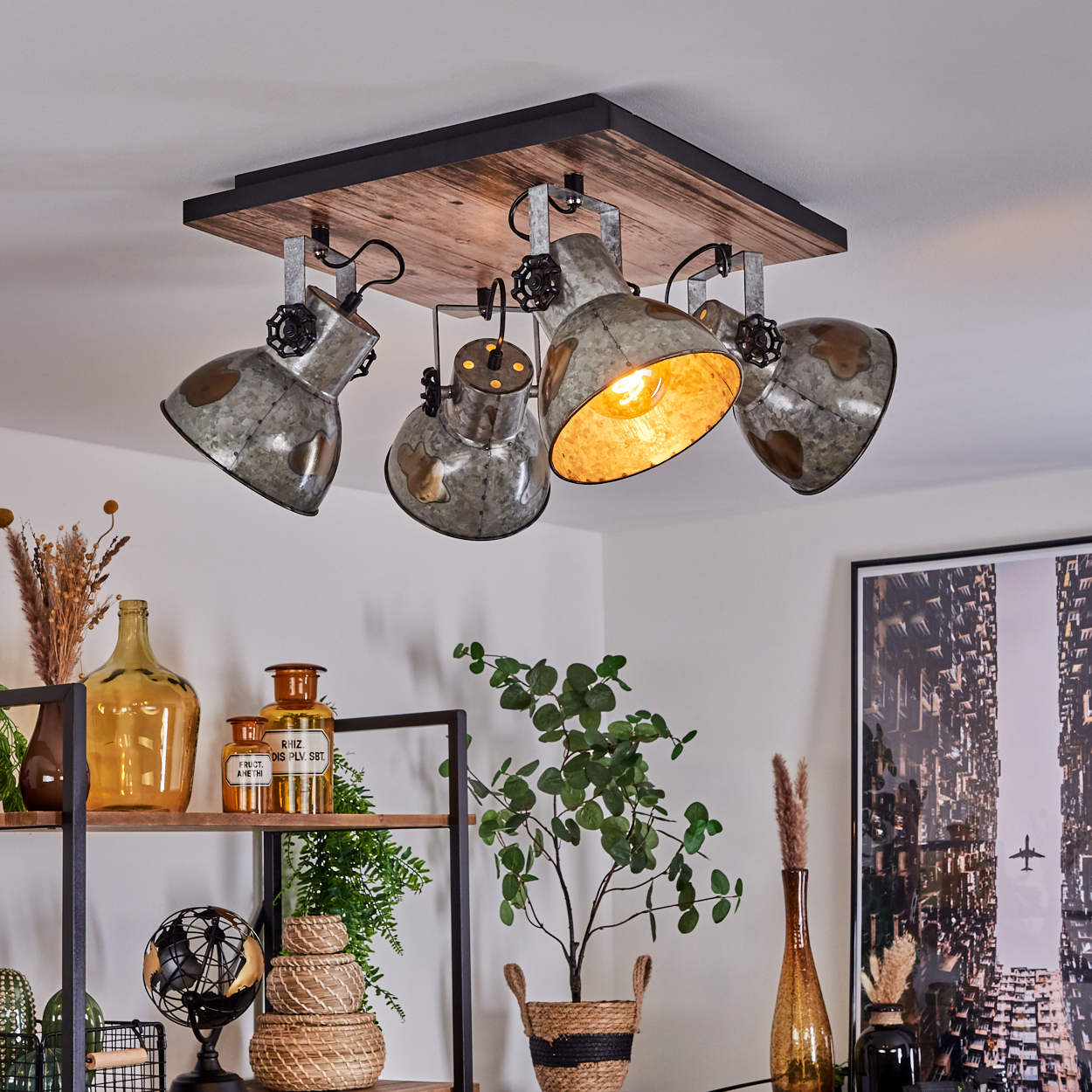 Deckenleuchte mit vier Metalllampen. Darunter Regale mit Flaschen, Pflanzen und einem Globus. Rechts ein Stadtbild.