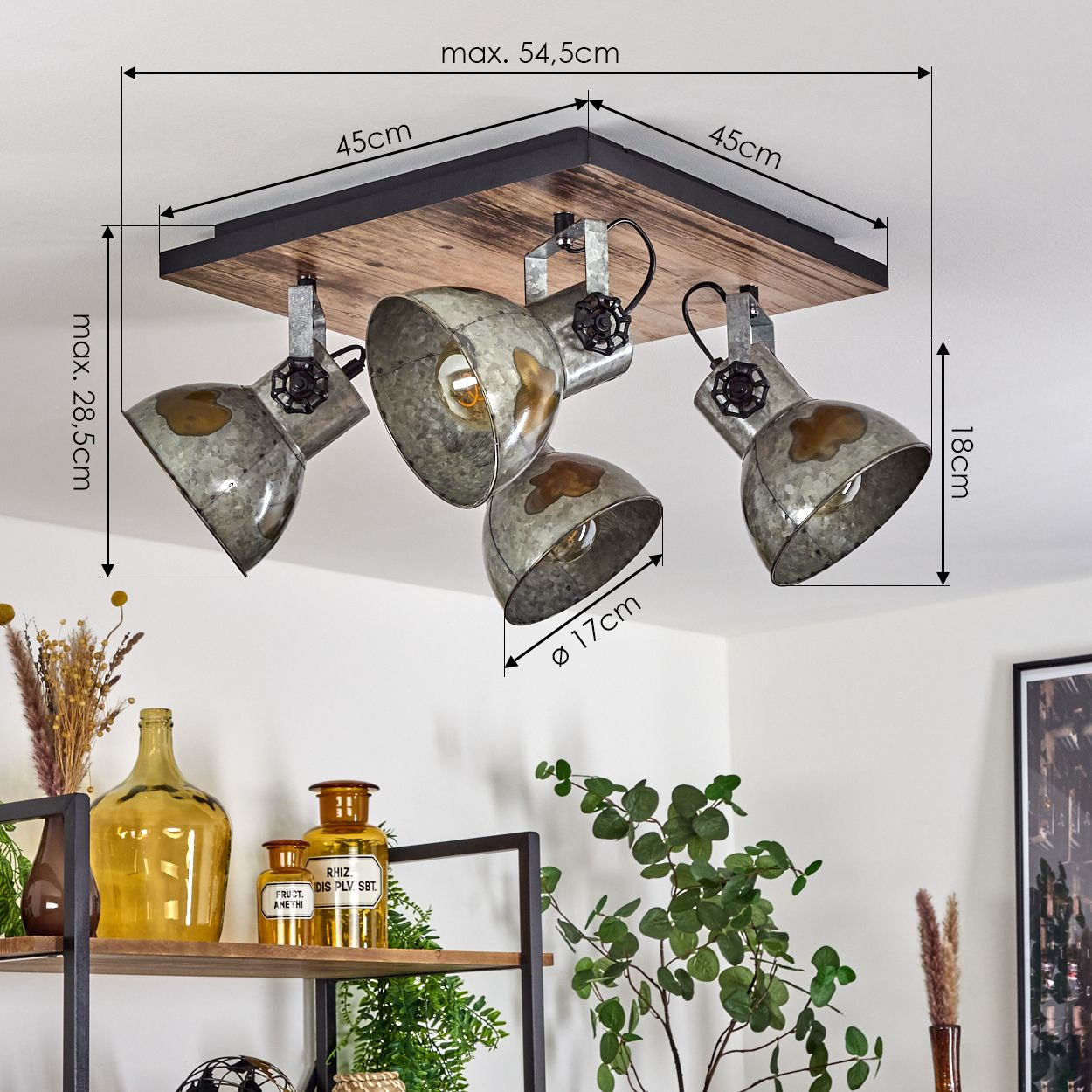 Deckenlampe mit drei Metall-Strahlern auf Holzbasis. Die Lampen sind nach unten gerichtet. Regale mit Flaschen und Pflanzen sind im Hintergrund.