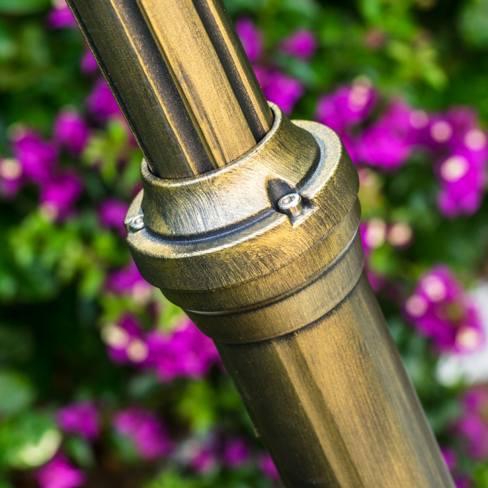 Nahaufnahme einer bronzefarbenen Metallstruktur mit dekorativem Ring. Verschwommener Hintergrund mit lila Blumen und grünem Laub.