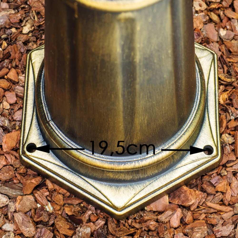 Ein bronzefarbener Metallsockel mit einem Maß von 19,5 cm, auf einem Bett aus braunen Holzspänen, Nahaufnahme.