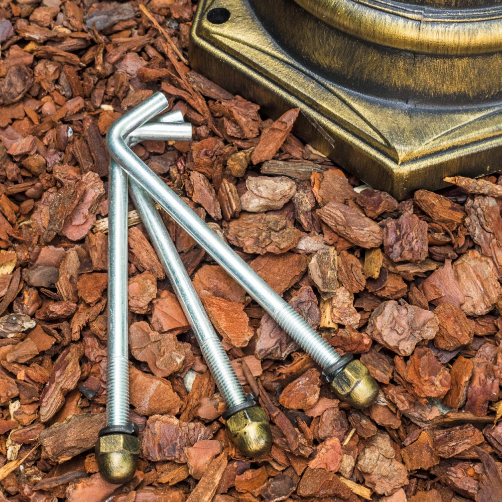 Drei Metallbolzen mit goldfarbenen Enden liegen auf braunen Holzschnitzeln, in der Nähe eines bronzefarbenen Sockels.