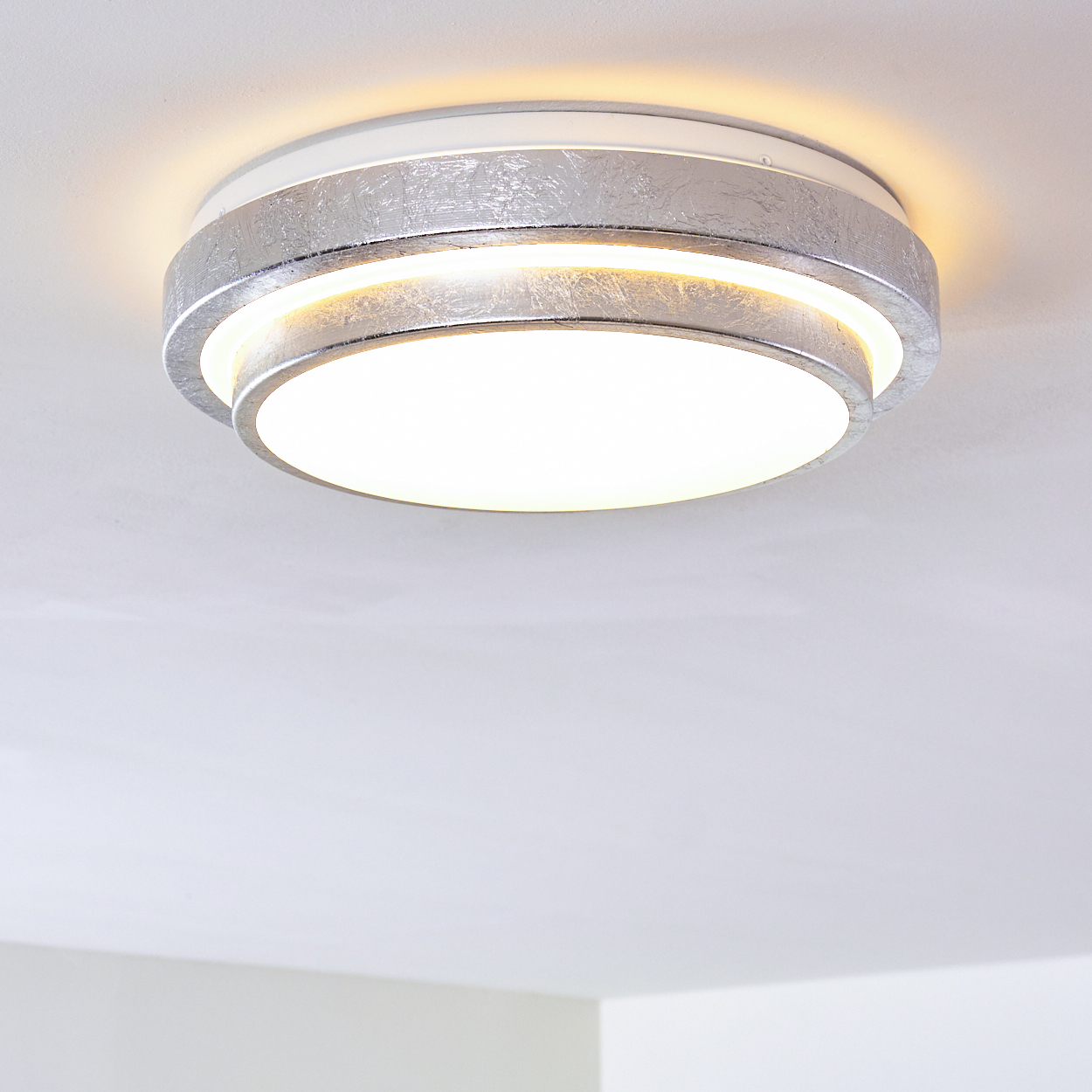 Eine runde, silberne Deckenleuchte ist an einer weißen Decke montiert. Das Licht hat eine helle, weiße Mittelscheibe.