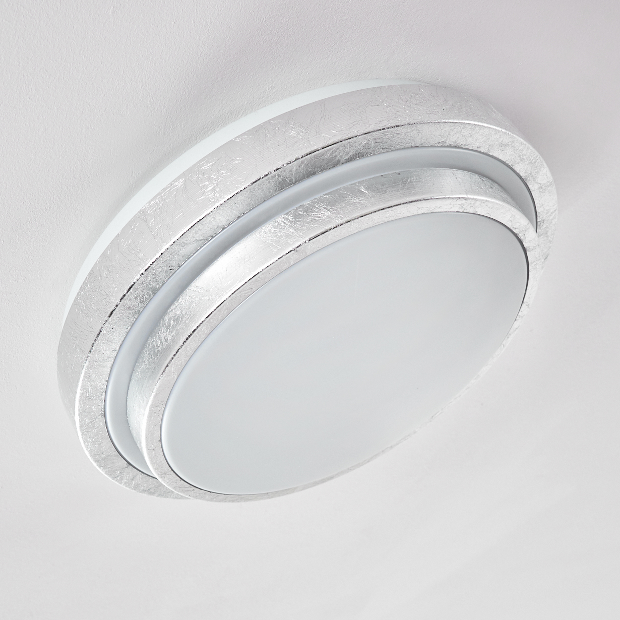Eine moderne Deckenleuchte, silber und weiß, oval geformt. Das Licht besteht aus konzentrischen Kreisen. Sie ist an einer weißen Decke montiert.